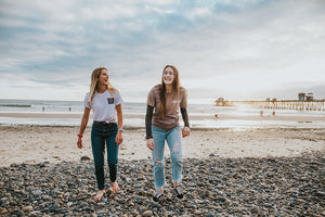 Two blond-haired women walking on the beach wearing the vegan and reef-safe NÖZ sunscreen on their noses. 